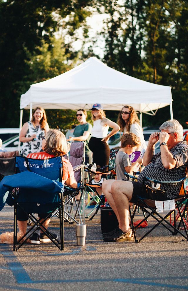 Fans in folding chairs under a canopy tent at a parking lot tailgate