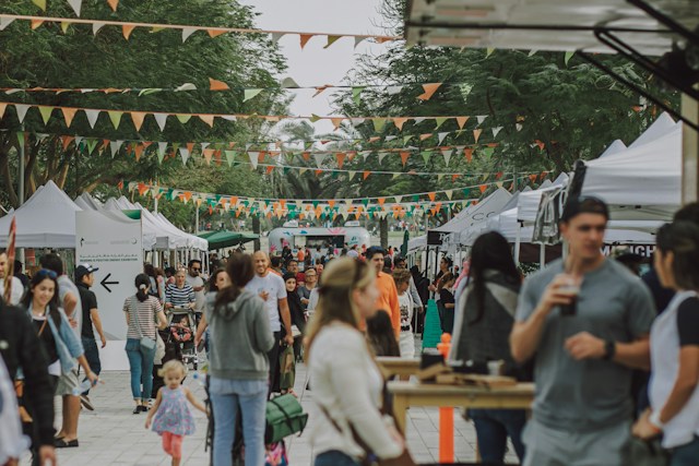 Crowd walking between white vendor tents under bunting at an outdoor fall festival