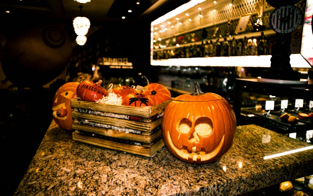 Carved jack-o'-lantern and a crate of small pumpkins on a bar counter at a Halloween party
