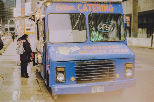 Customer ordering at the service window of a blue food truck on a city street