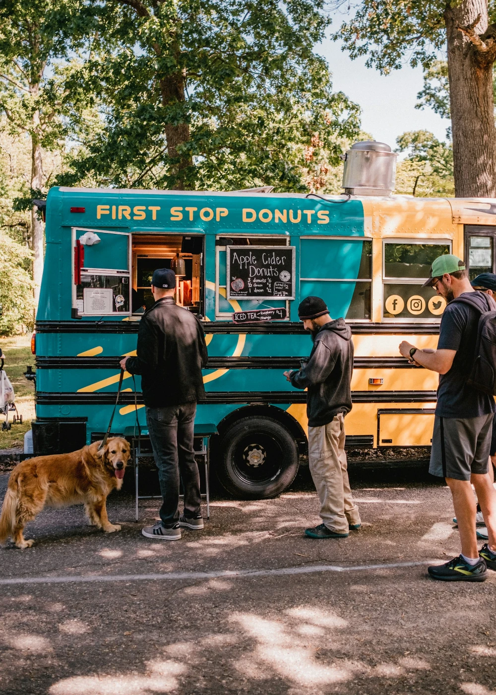 Customers lining up at a converted school bus food truck in a park